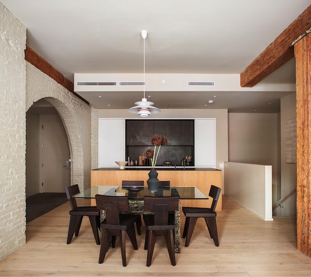 dining area with brick wall, arched walkways, visible vents, and light wood finished floors