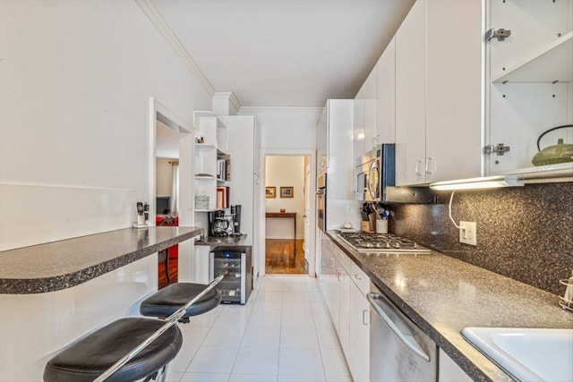 kitchen with beverage cooler, light tile patterned flooring, white cabinets, appliances with stainless steel finishes, and crown molding