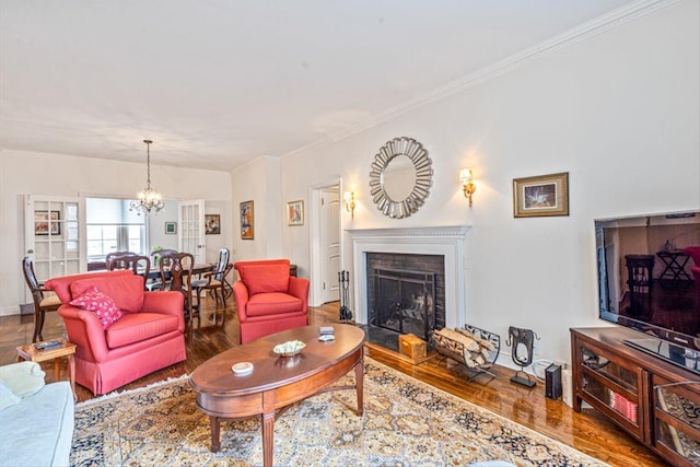 living room featuring wood finished floors, baseboards, a fireplace, ornamental molding, and a chandelier