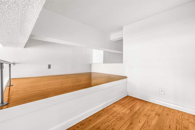 empty room with a textured ceiling, baseboards, and wood finished floors