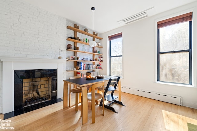 dining room featuring visible vents, a fireplace, light wood-type flooring, and a baseboard radiator