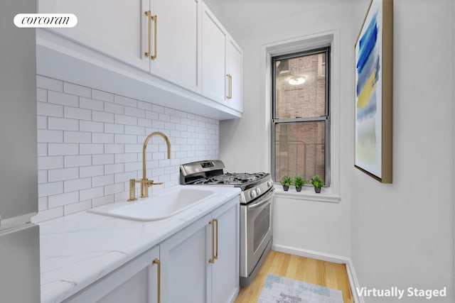kitchen with light wood-type flooring, stainless steel gas range oven, white cabinets, light stone countertops, and a sink