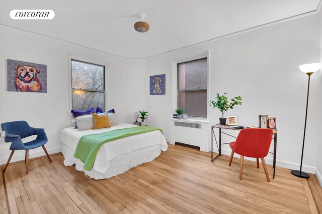 bedroom with radiator heating unit, visible vents, baseboards, and wood finished floors