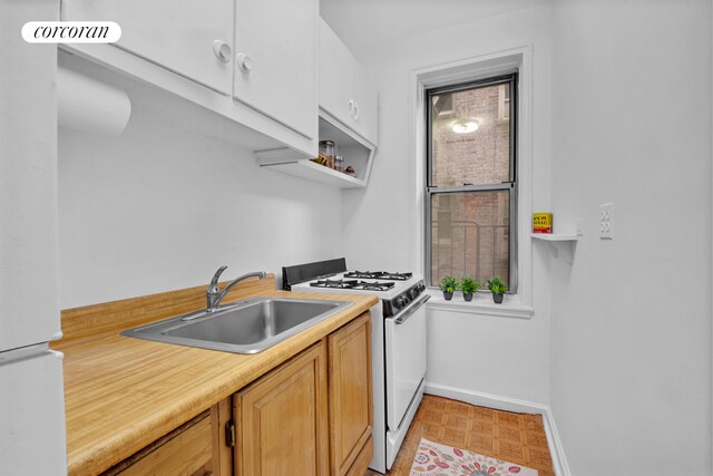 kitchen with baseboards, a sink, light countertops, white range with gas cooktop, and light floors