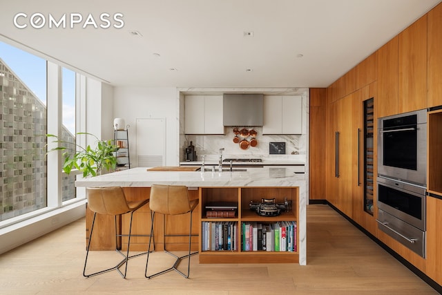 kitchen featuring wall chimney range hood, a warming drawer, modern cabinets, and tasteful backsplash