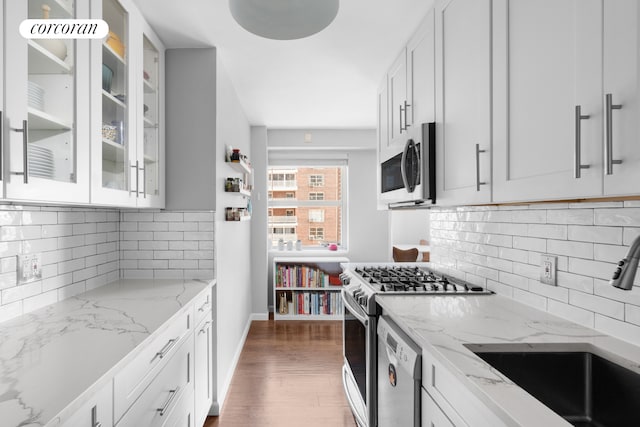 kitchen featuring light stone counters, gas stove, a sink, glass insert cabinets, and stainless steel microwave