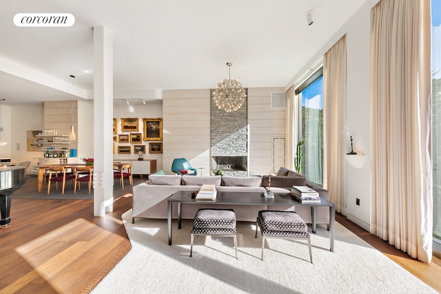 living room with visible vents, a notable chandelier, wood finished floors, a large fireplace, and wood walls