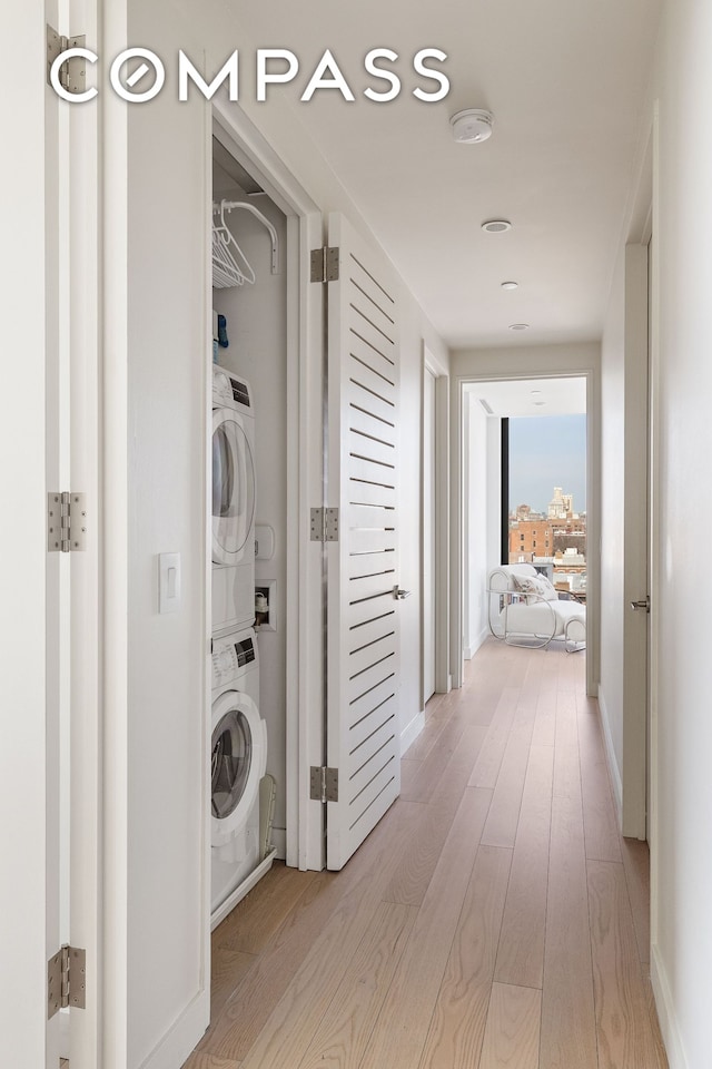 clothes washing area with baseboards, light wood finished floors, laundry area, and stacked washing maching and dryer