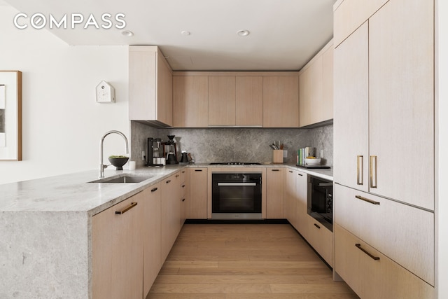 kitchen with a sink, black appliances, a peninsula, and light brown cabinets