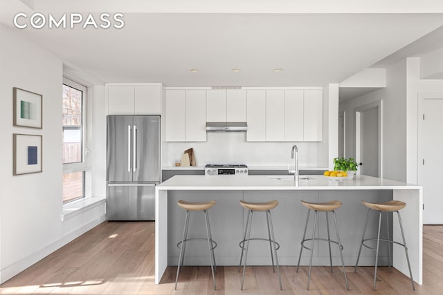 kitchen featuring stainless steel refrigerator, a sink, under cabinet range hood, white cabinets, and range