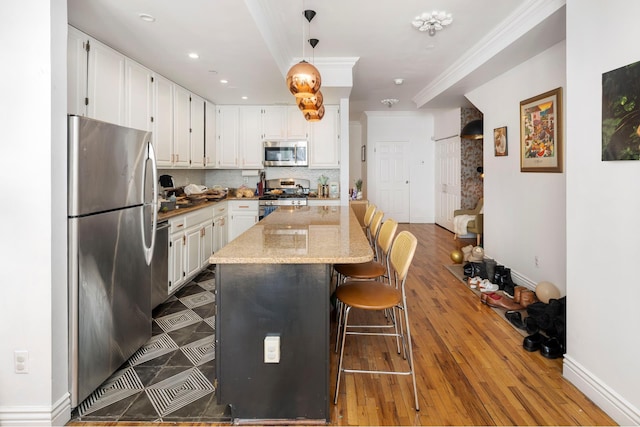 kitchen featuring backsplash, appliances with stainless steel finishes, white cabinetry, crown molding, and a kitchen bar