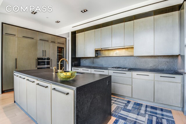 505 W 19th St Unit 7W, New York City, NY 10011 - kitchen featuring light wood finished floors, tasteful backsplash, appliances with stainless steel finishes, a center island with sink, and dark countertops