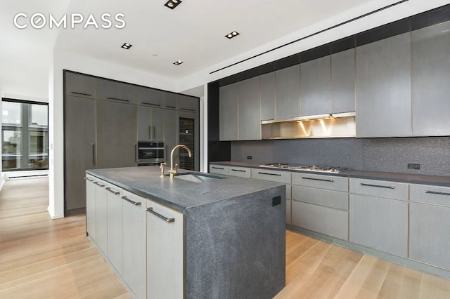 kitchen featuring a sink, backsplash, light wood-style floors, stainless steel appliances, and modern cabinets