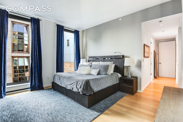 bedroom with a baseboard radiator, baseboards, and wood finished floors