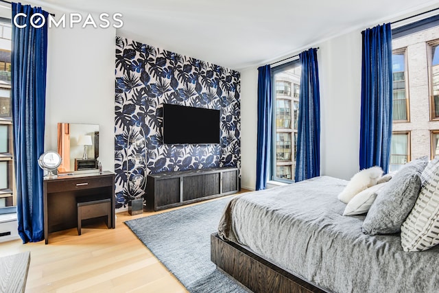 bedroom with an accent wall, wood finished floors, and wallpapered walls