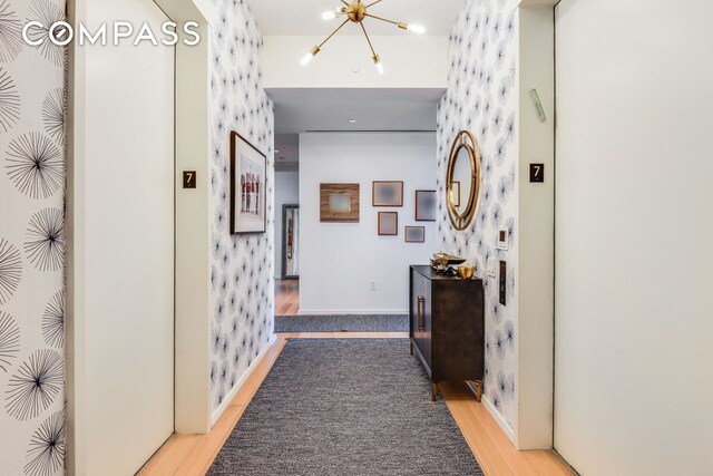 505 W 19th St Unit 7W, New York City, NY 10011 - corridor with a chandelier, baseboards, wallpapered walls, wood finished floors, and elevator