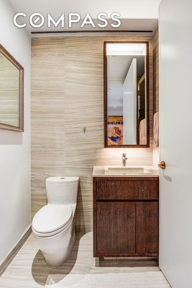 half bath featuring vanity, tile walls, and toilet