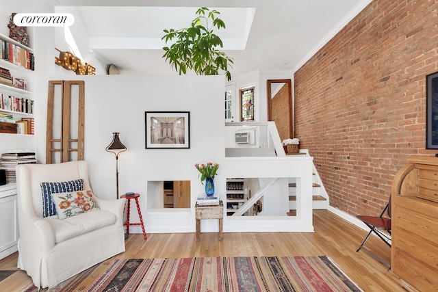 living area featuring crown molding, a wall mounted air conditioner, wood finished floors, and brick wall