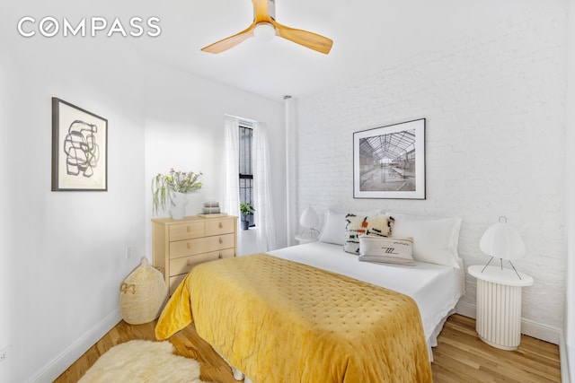 bedroom with brick wall, a ceiling fan, baseboards, and wood finished floors