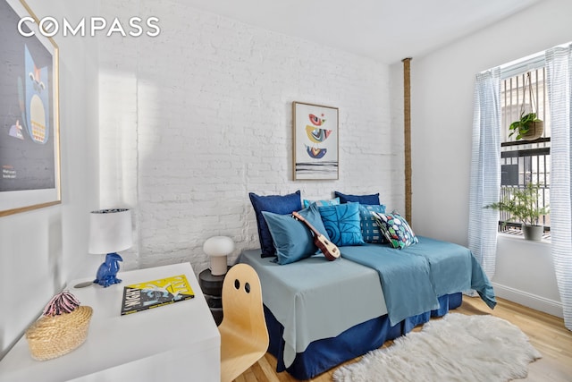 bedroom with wood finished floors and brick wall