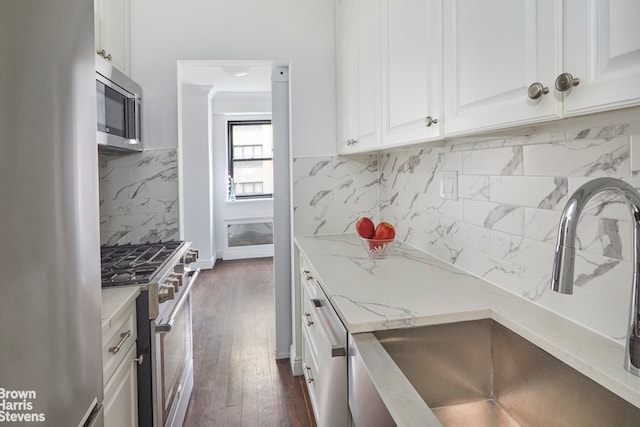 kitchen featuring tasteful backsplash, light stone counters, stainless steel appliances, white cabinetry, and a sink