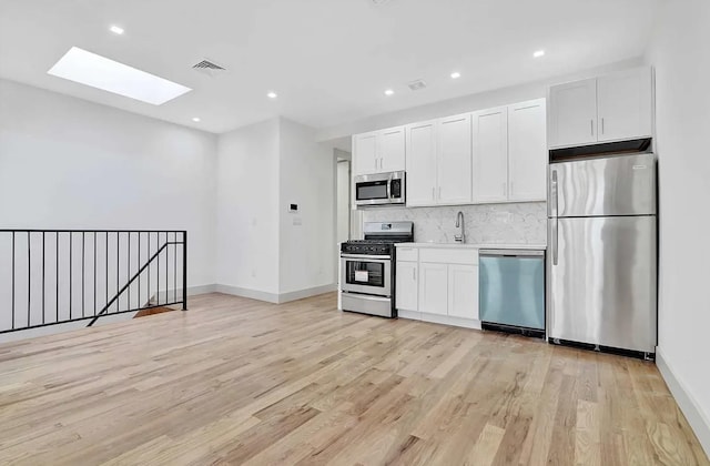 282 E 38th St, New York City, NY 11203 - kitchen featuring stainless steel appliances, a skylight, a sink, backsplash, and light wood-style floors