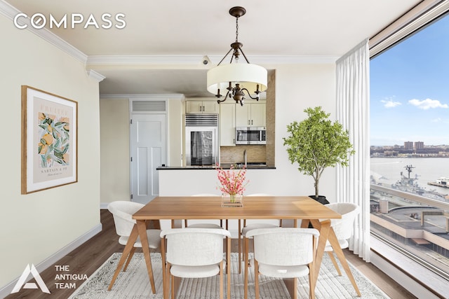 dining area with wood finished floors, baseboards, ornamental molding, a water view, and a chandelier