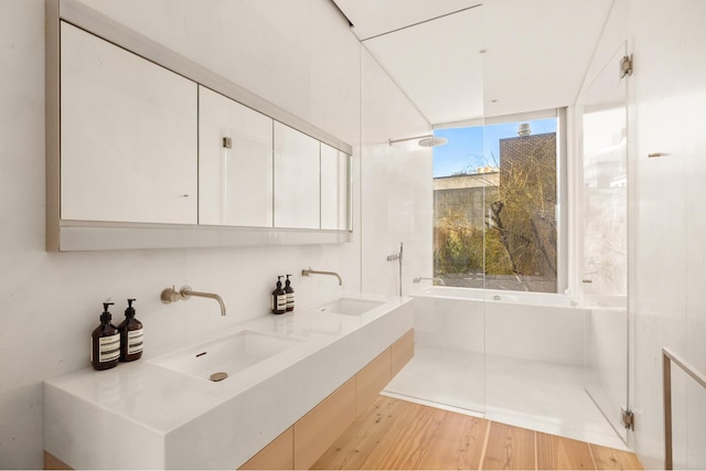 full bath featuring walk in shower, wood finished floors, a tub, and a sink