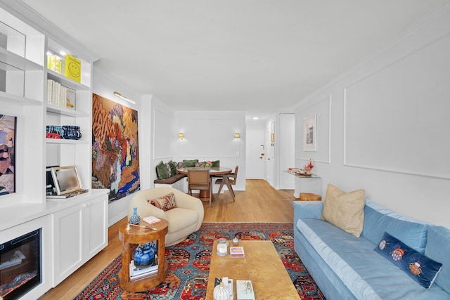 living area with crown molding, light wood-style flooring, and a decorative wall