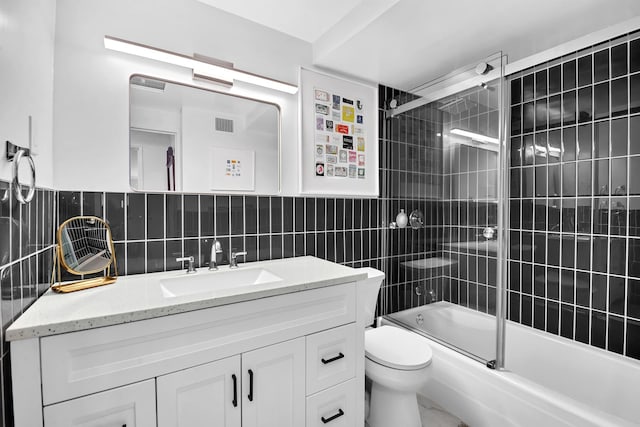 full bathroom featuring toilet, tile walls, vanity, and bath / shower combo with glass door