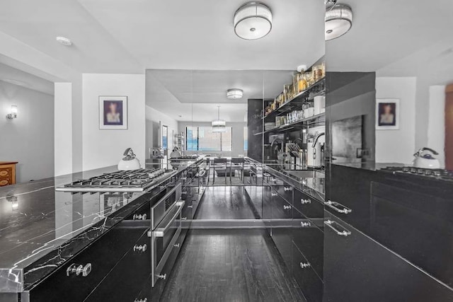 kitchen featuring open shelves, a sink, dark countertops, wood finished floors, and stainless steel gas stovetop