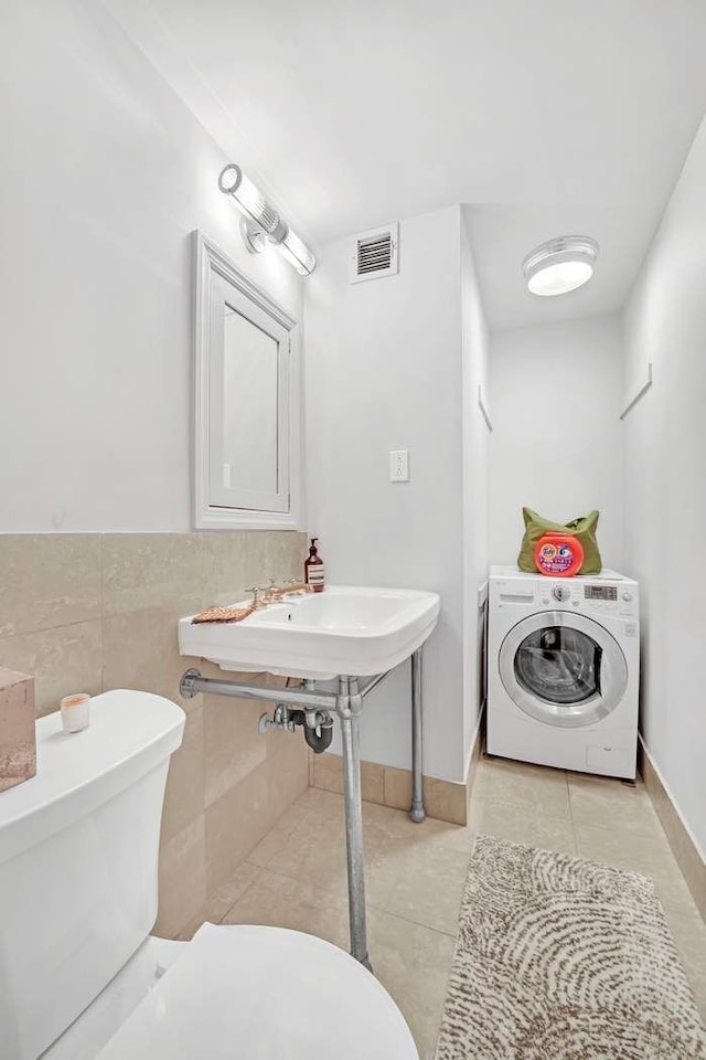 half bathroom with tile patterned flooring, visible vents, toilet, washer / dryer, and tile walls