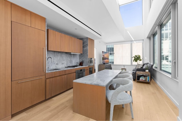 kitchen with a breakfast bar area, stainless steel gas stovetop, a sink, and light wood-style flooring
