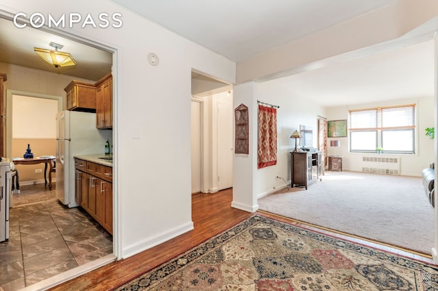 interior space featuring brown cabinetry, radiator, freestanding refrigerator, baseboards, and open floor plan