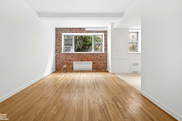 empty room featuring radiator heating unit, light wood-type flooring, and baseboards