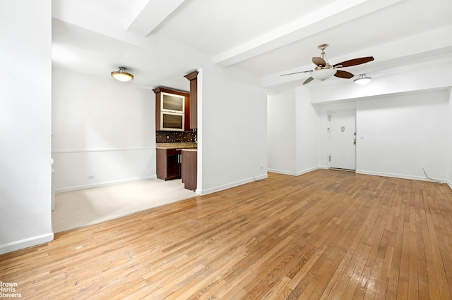 unfurnished living room featuring light wood finished floors, beamed ceiling, baseboards, and ceiling fan