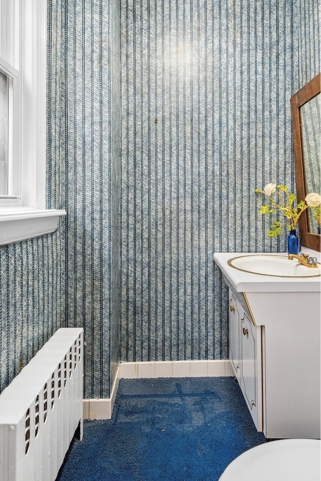 bathroom featuring wallpapered walls, radiator heating unit, vanity, and baseboards