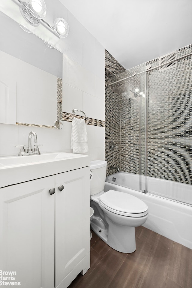 bathroom with combined bath / shower with glass door, toilet, wood finished floors, and vanity