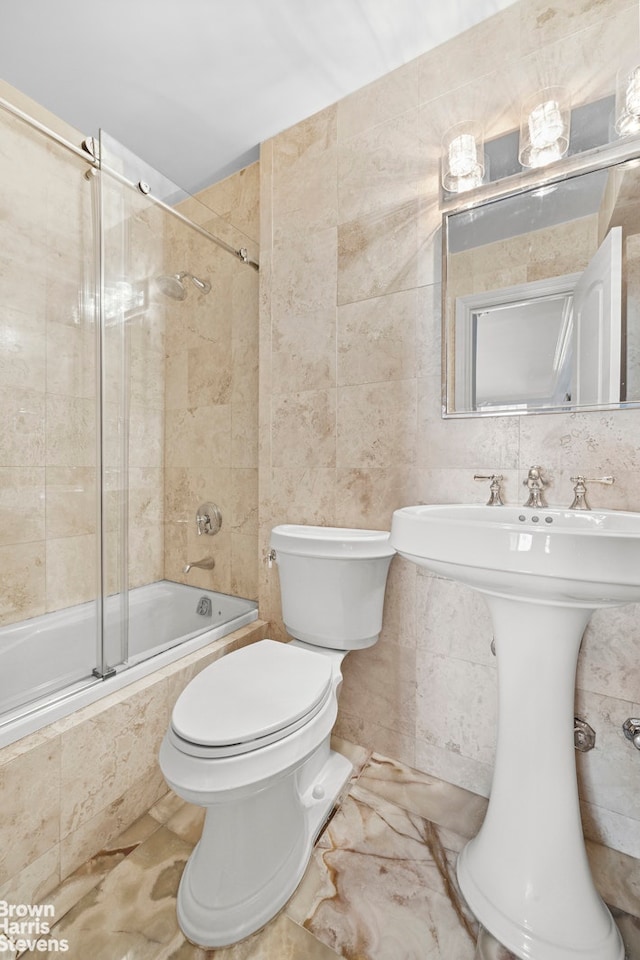 full bath featuring toilet, tiled shower / bath, tile walls, and a sink