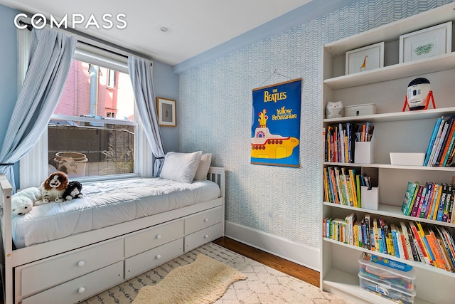 bedroom with wallpapered walls, an accent wall, baseboards, and wood finished floors