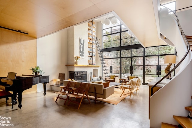 living area with a glass covered fireplace, a high ceiling, concrete floors, a wall of windows, and stairs