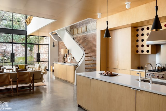 kitchen featuring light brown cabinets, a sink, decorative light fixtures, concrete floors, and light countertops