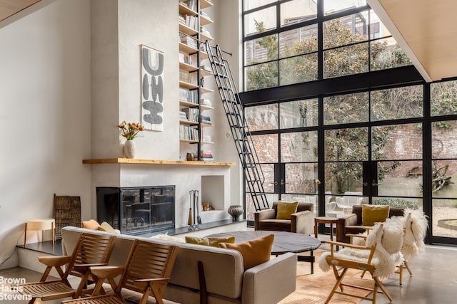 living room featuring floor to ceiling windows, a glass covered fireplace, and a towering ceiling