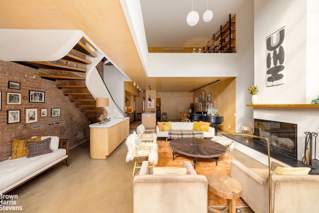 living area with a glass covered fireplace, a towering ceiling, concrete floors, and brick wall