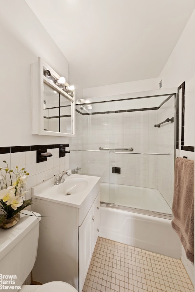 full bathroom with toilet, shower / bath combination with glass door, tile walls, tile patterned flooring, and vanity