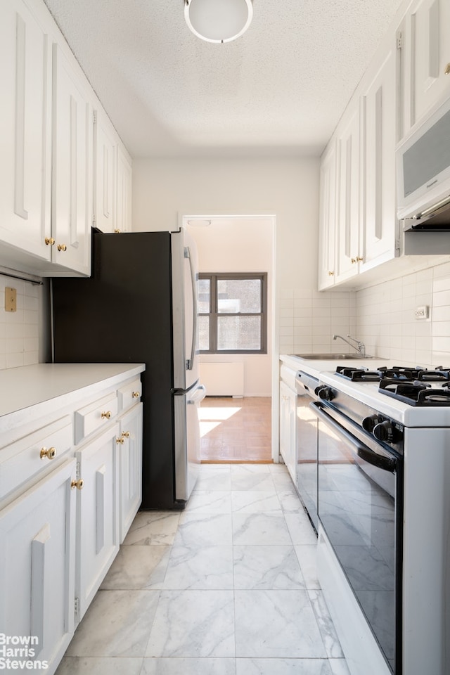 kitchen with tasteful backsplash, light countertops, stainless steel appliances, marble finish floor, and white cabinetry