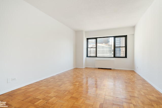 unfurnished room with radiator, a textured ceiling, and baseboards