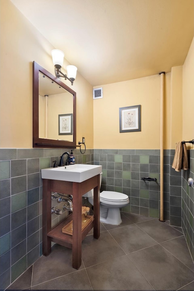 half bathroom featuring tile patterned floors, visible vents, toilet, and tile walls