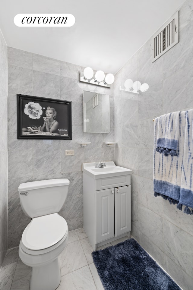 half bath with visible vents, toilet, vanity, marble finish floor, and tile walls