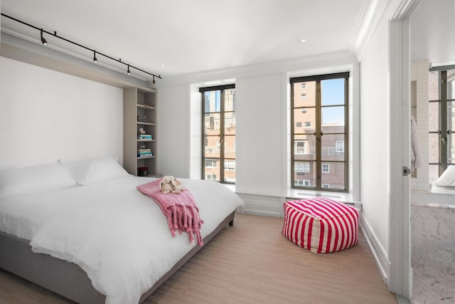 bedroom with wood finished floors, crown molding, and multiple windows